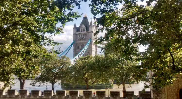 One of Tower Bridge's towers peeps through a gap in the trees, with the battlements of the Tower of London in the foreground